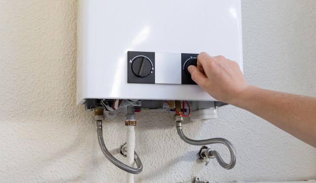 A hand adjusting the temperature dial on a modern water heater mounted on a wall.