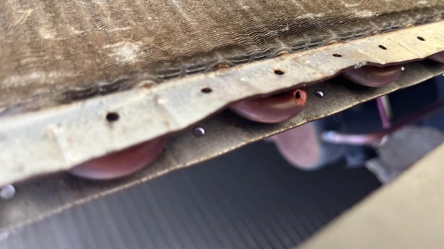 Close-up of a metal cooling coil with a hole, some rust and discoloration, revealing wear over time.