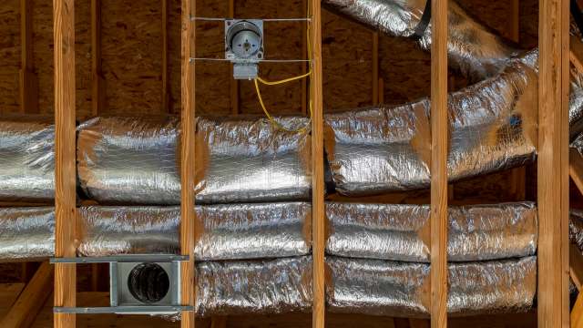 Insulated ductwork is mounted within wooden framing in a construction setting.