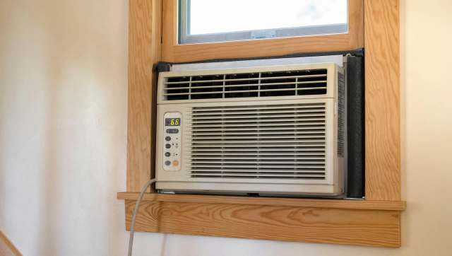 A window air conditioning unit installed in a wooden frame with a digital display showing 66 degrees.