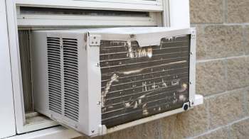 An air conditioning unit partially installed in a window, showing dirt and wear on the exterior.