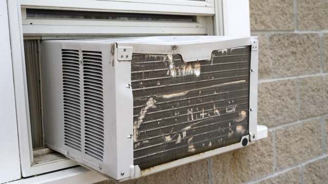 An air conditioning unit partially installed in a window, showing dirt and wear on the exterior.