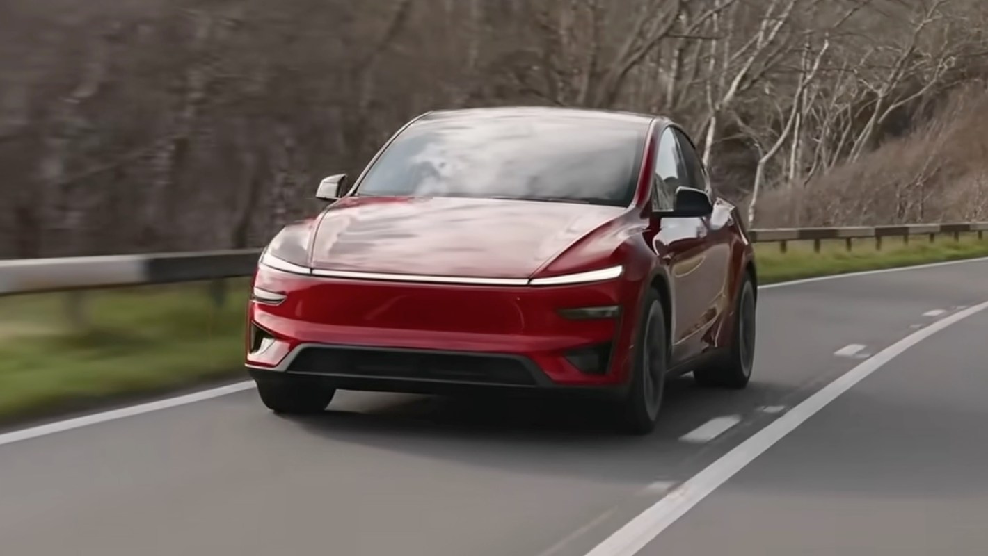 A red EV driving on a road surrounded by bare trees.