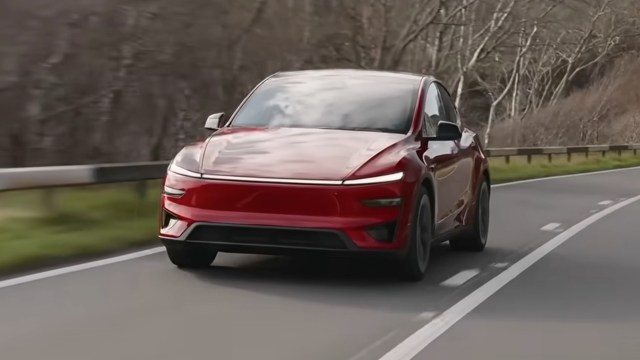 A red EV driving on a road surrounded by bare trees.
