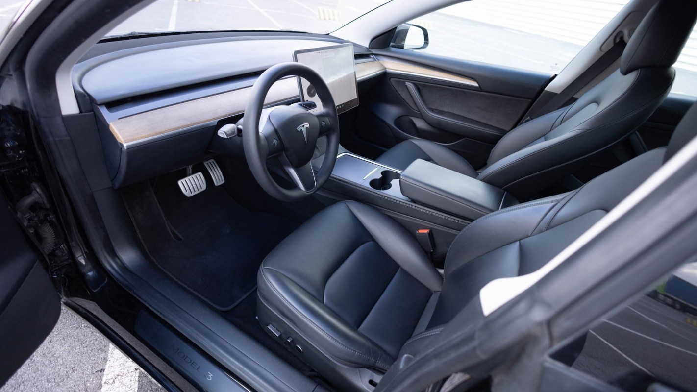 An interior of a Tesla Model 3 with black leather seats and a central touchscreen.
