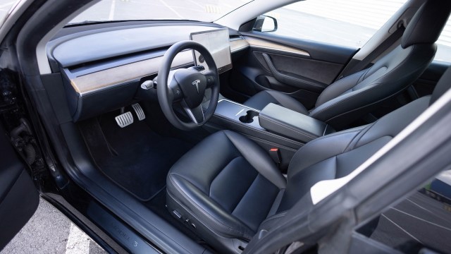 An interior of a Tesla Model 3 with black leather seats and a central touchscreen.