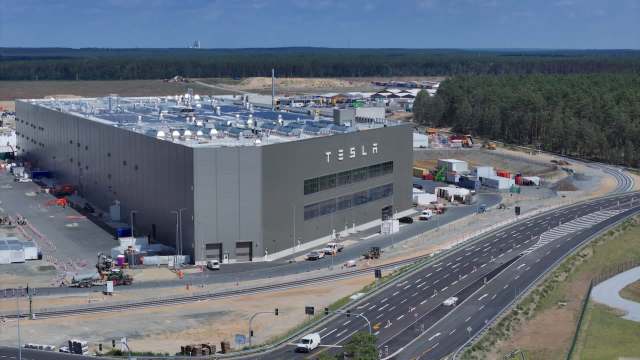 A large Tesla factory building in Berlin with construction activity and vehicles in the surrounding area on a sunny day.