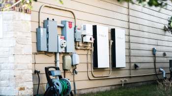 A side view of an exterior wall featuring electrical panels and Tesla energy storage units.