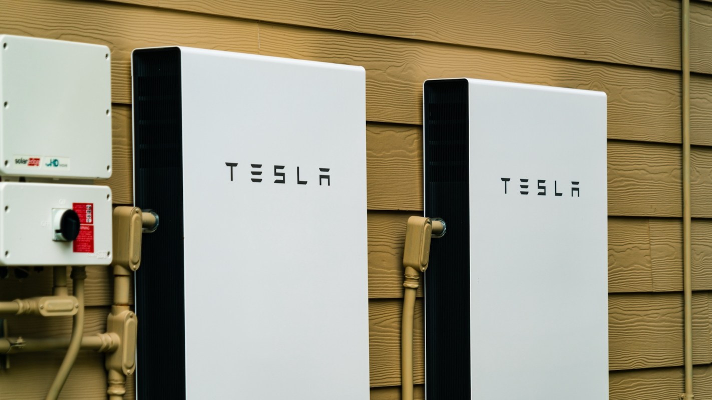 Two Tesla wall batteries mounted on a beige wall, alongside a solar inverter.