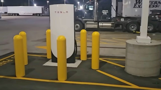 A Tesla charging station surrounded by yellow safety poles at a truck parking area.