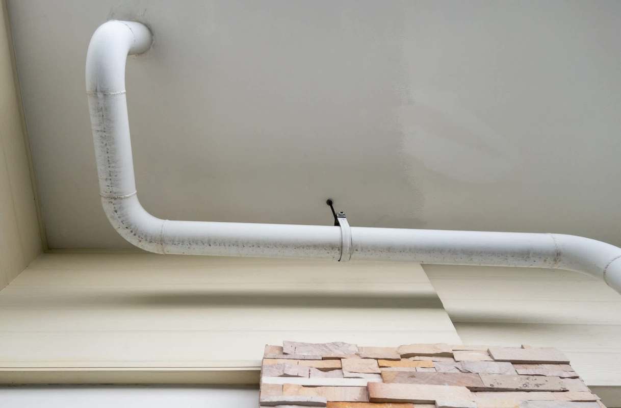 A white pipe curves along the ceiling above a textured stone wall.