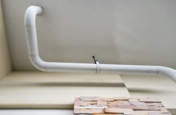 A white pipe curves along the ceiling above a textured stone wall.