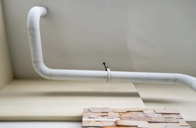 A white pipe curves along the ceiling above a textured stone wall.