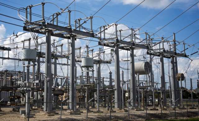An electrical substation with metal structures, wires, and equipment under a cloudy sky.