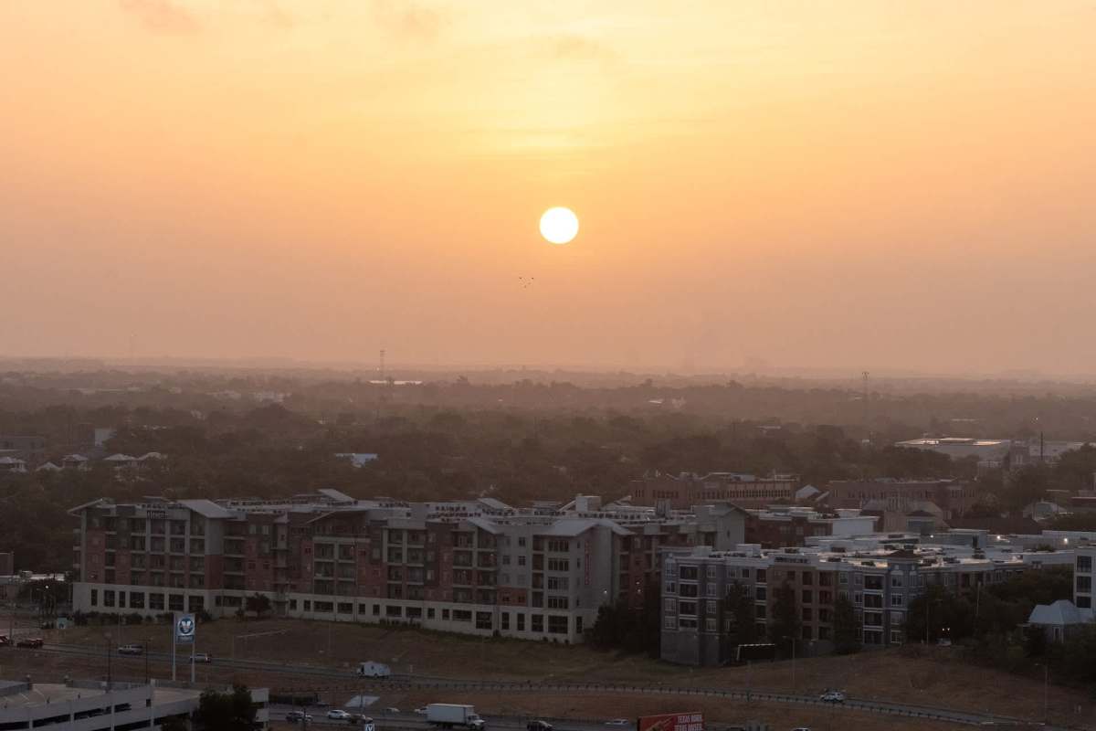 A sunset view over a suburban landscape, featuring buildings and a highway in the foreground.