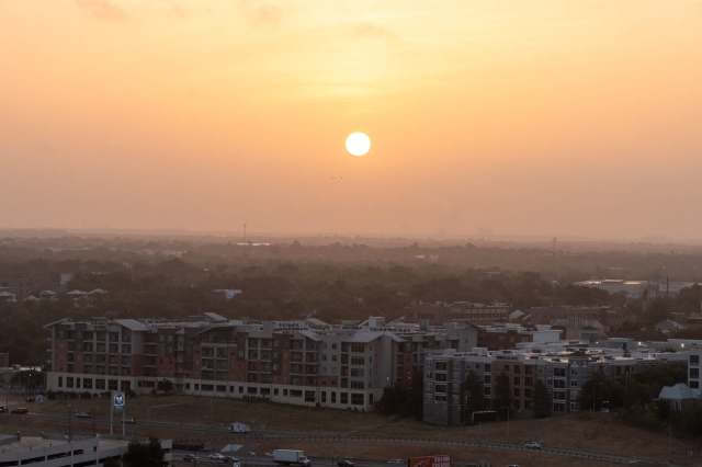 A sunset view over a suburban landscape, featuring buildings and a highway in the foreground.