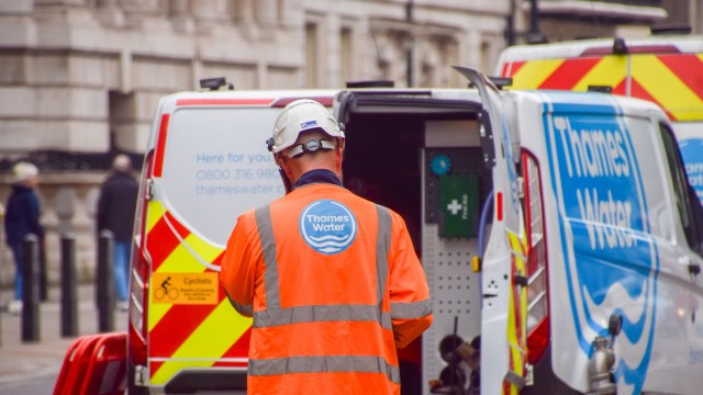 A worker in an orange Thames Water jacket inspects a service van on a city street.