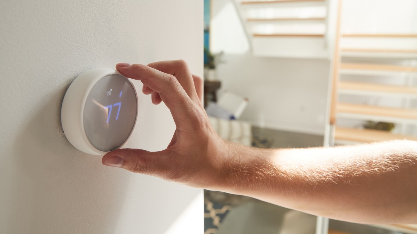 A person adjusts a smart thermostat displaying the temperature setting in a modern home interior.