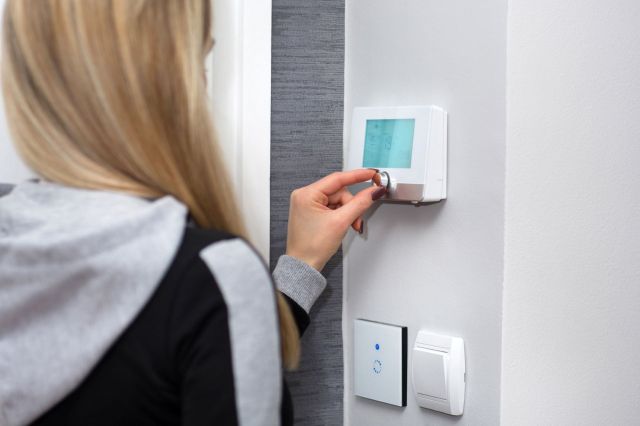 A person adjusting a digital thermostat on a wall.