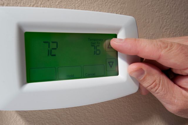 A person adjusting their thermostat.