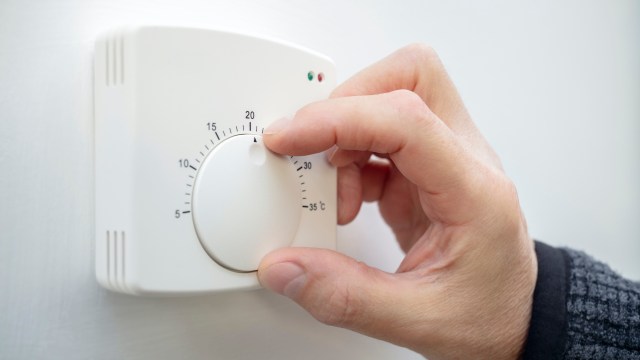 A hand adjusts the temperature dial on a white thermostat displaying numeric values.