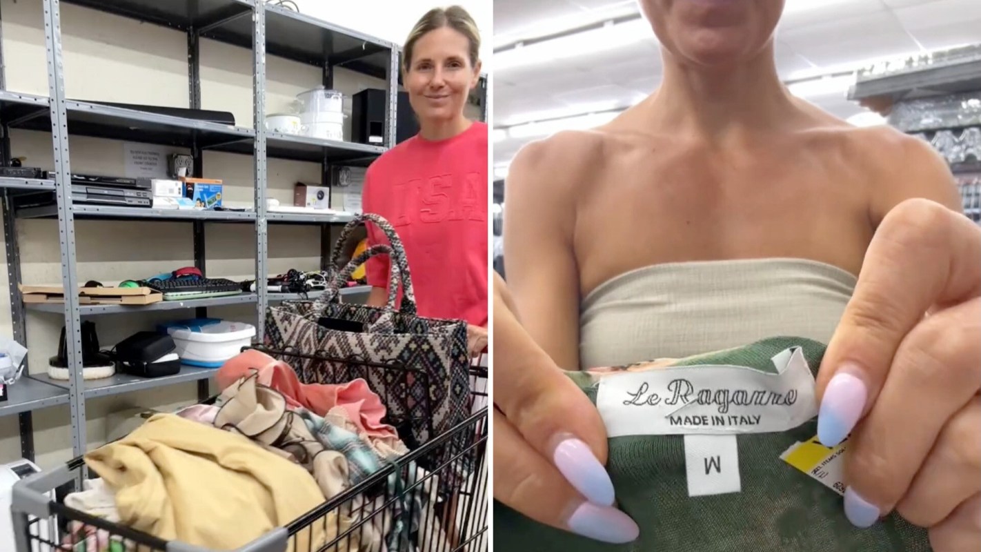 A woman smiles while holding a shopping cart filled with clothing in a thrift store.