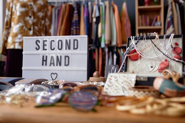 A display of second-hand jewelry and accessories with a lightbox sign reading "SECOND HAND" in a boutique setting.