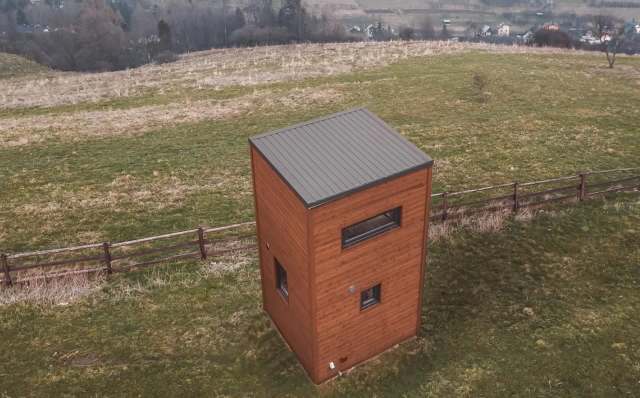 A skyscraper-shaped tiny home in a field.
