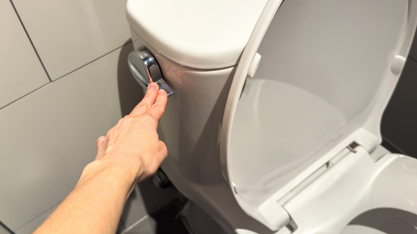 A hand flushing an open toilet.