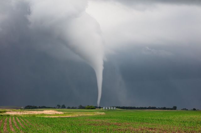 A tornado descends from storm clouds over a farm field.