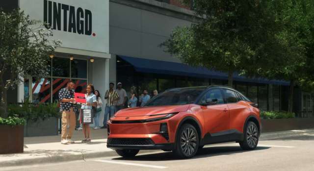 An orange electric car parked in front of a retail store.