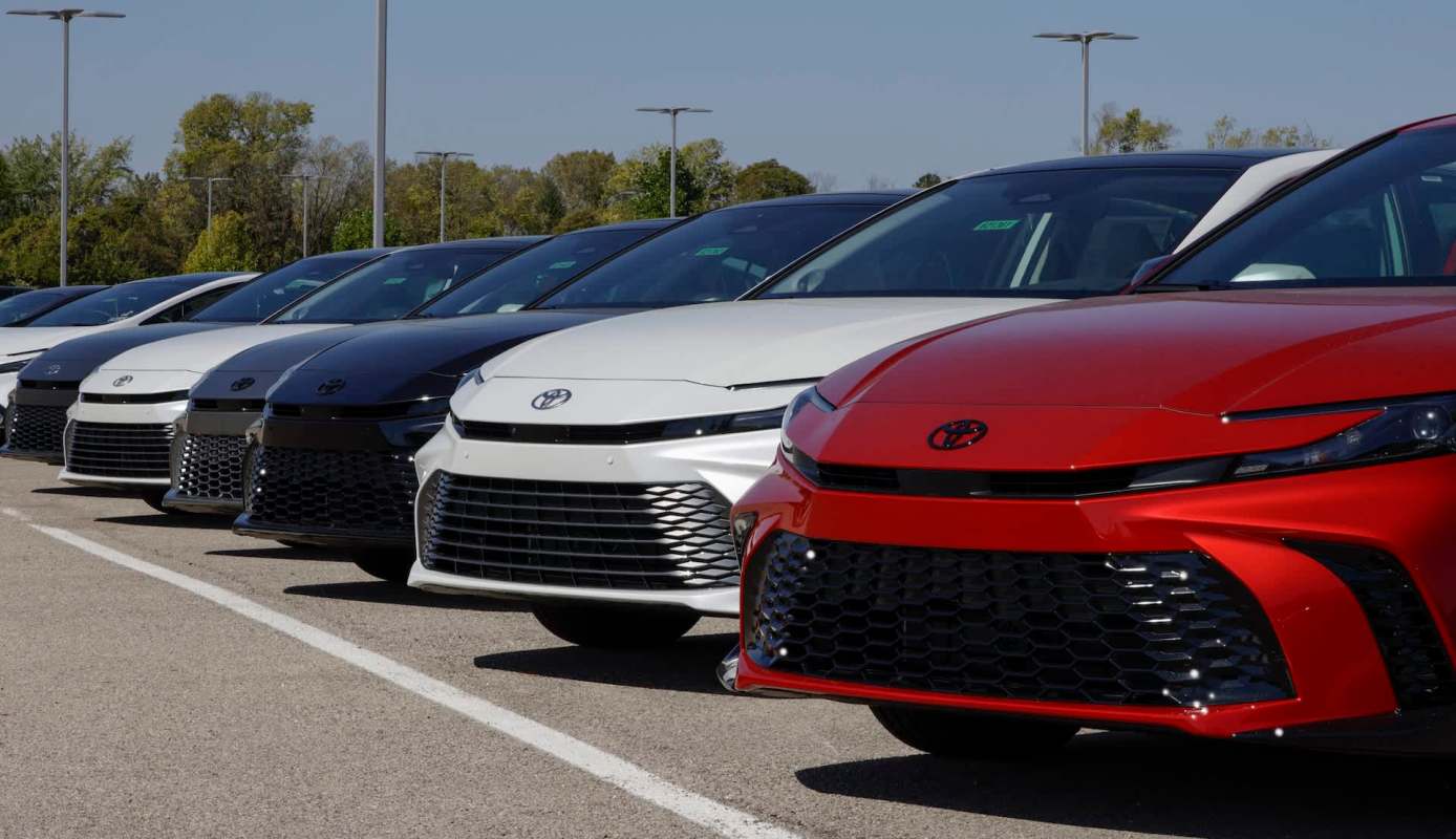 A line of new Toyota cars in various colors parked under clear blue skies.