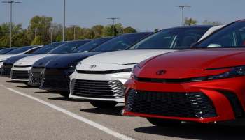 A line of new Toyota cars in various colors parked under clear blue skies.