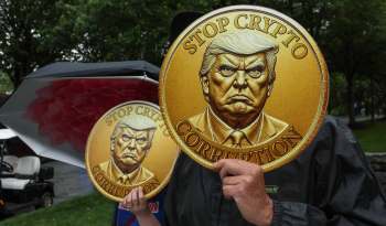 Protesters hold large coins with an anti-crypto message and a stern figure of President Trump's likeness in a park.