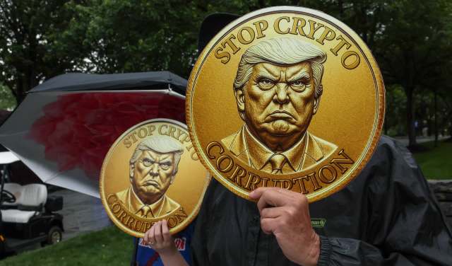 Protesters hold large coins with an anti-crypto message and a stern figure of President Trump's likeness in a park.