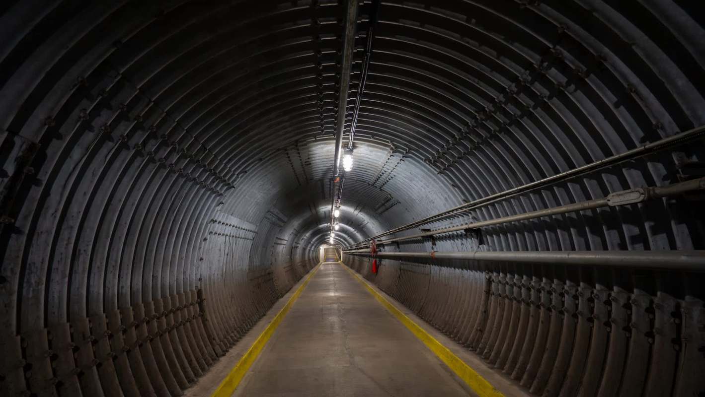 A long, dimly lit tunnel with curved metal walls and yellow safety lines on the floor.