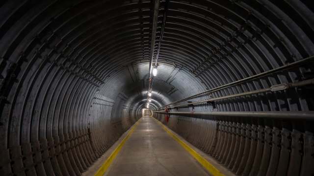 A long, dimly lit tunnel with curved metal walls and yellow safety lines on the floor.