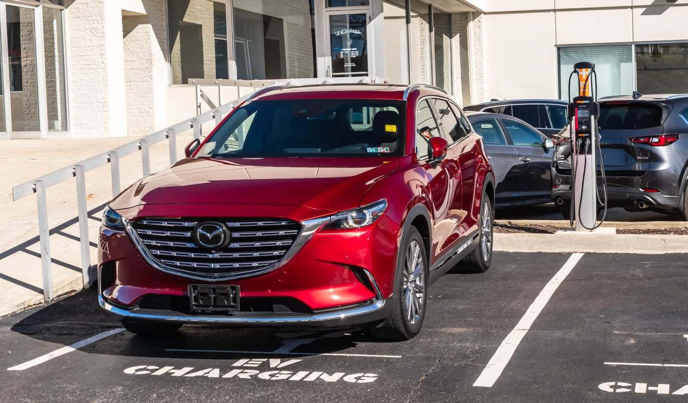 A red Mazda SUV parked in an EV charging space next to a charging station.