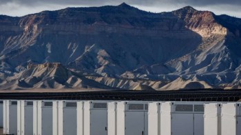 White storage units lined up in the foreground with a rugged mountain landscape in the background under a cloudy sky.