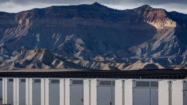 White storage units lined up in the foreground with a rugged mountain landscape in the background under a cloudy sky.
