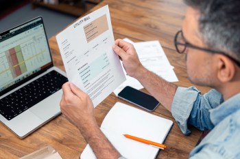 A person reviewing a utility bill while sitting at a desk with a laptop and notepad.