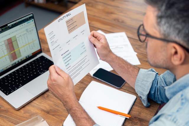 A person reviewing a utility bill while sitting at a desk with a laptop and notepad.
