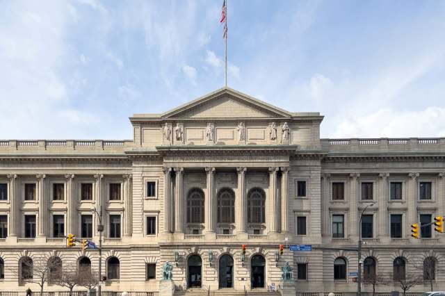 A grand courthouse building with classical architecture, featuring statues and an American flag.