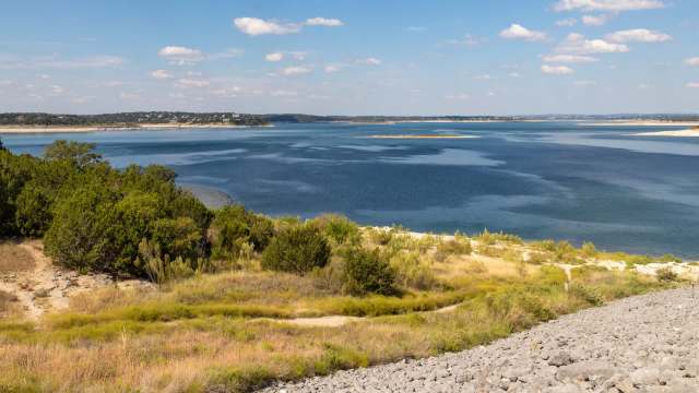 A view of a lake surrounded by vegetation and rocky shorelines under a clear blue sky.