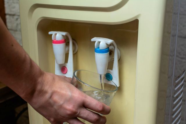 A person filling a glass from a water dispenser.