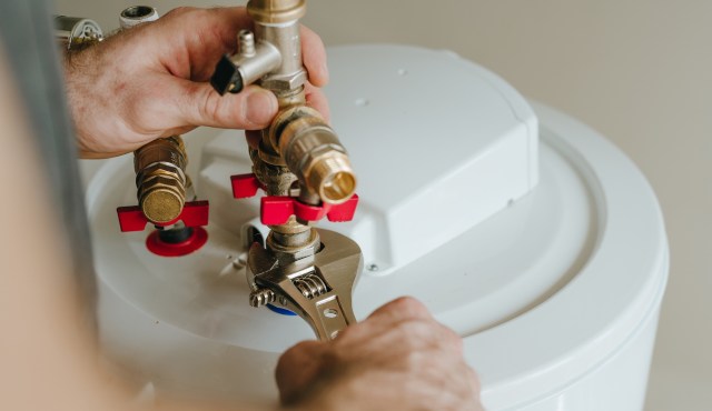 A person uses a wrench to adjust plumbing valves on a water heater.