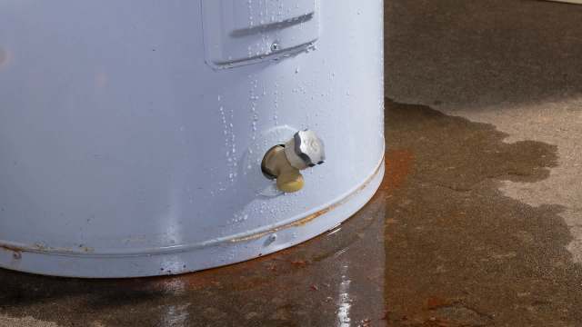 A water heater with a valve and water pooling on the floor, indicating a possible leak.