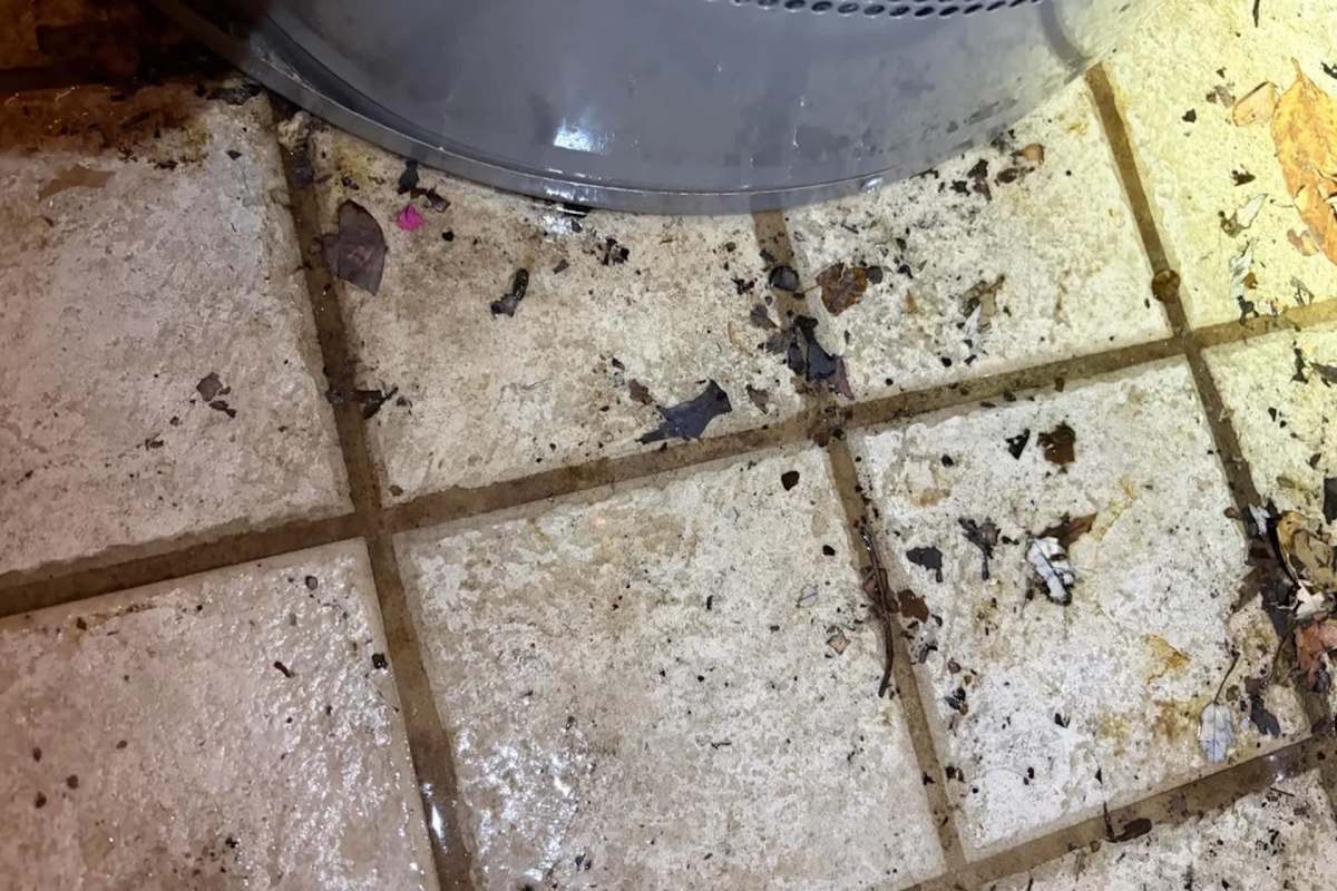 A dirty floor with debris and a small pool of water near a gray water heater.
