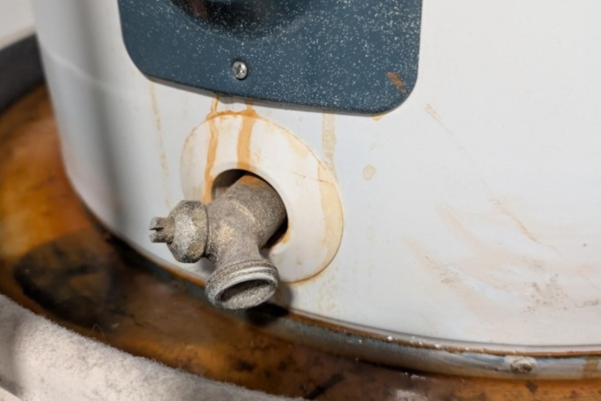 A close-up of a rusty water heater valve with visible stains around the fitting.