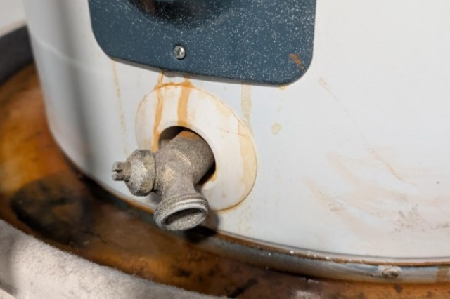A close-up of a rusty water heater valve with visible stains around the fitting.